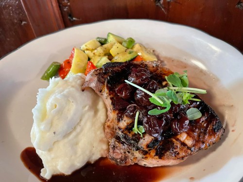 Grilled chicken breast topped with cherry sauce, served with mashed potatoes and sautéed vegetables on a white plate.