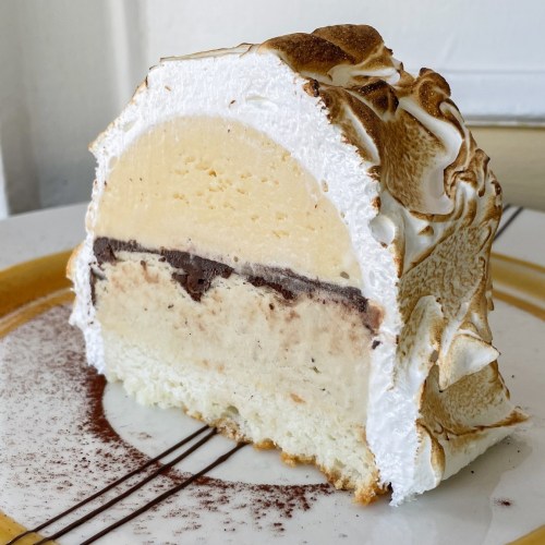 A slice of layered ice cream cake with chocolate, vanilla, and meringue topping on a decorative plate.