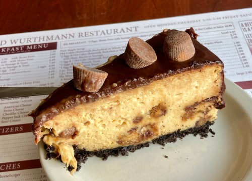 A slice of chocolate peanut butter cheesecake topped with chocolate and peanut butter cups on a plate.