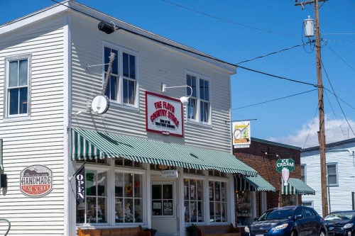 A quaint shop with a striped awning, featuring a sign that reads "The Flavor Country Store" and an "Open" sign.
