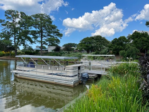 Two boats docked on a calm waterway, surrounded by lush greenery and trees under a partly cloudy sky.