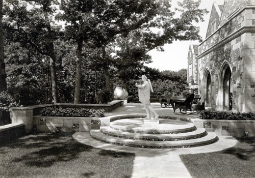 A serene garden scene featuring a statue on a circular stone platform, surrounded by trees and a grand building.