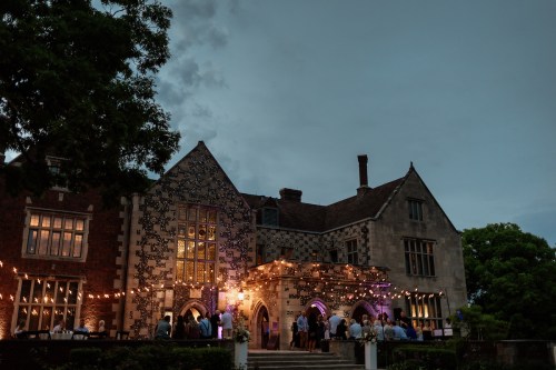 A beautifully lit historic mansion with guests mingling outside under a twilight sky.