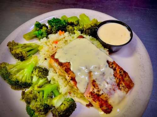 Grilled salmon with creamy sauce, served on a bed of rice and steamed broccoli on a white plate.
