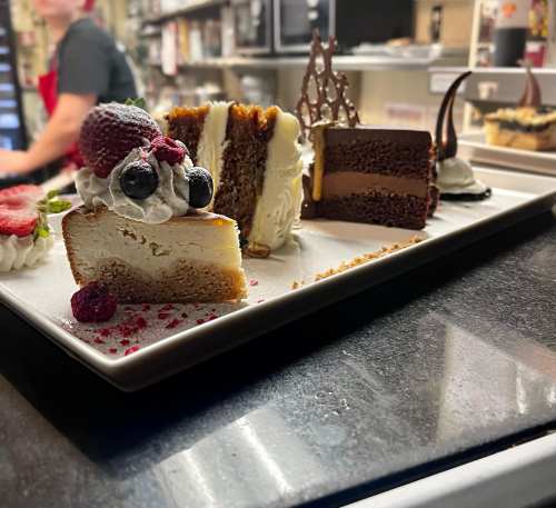 A platter of assorted desserts, including cheesecake, chocolate cake, and layered cake, garnished with berries and whipped cream.