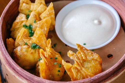 A bamboo steamer filled with golden fried dumplings and a small bowl of creamy dipping sauce.