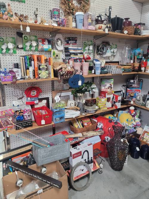 A cluttered thrift store shelf filled with various items, including books, kitchenware, and decorative objects.
