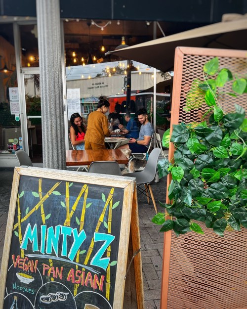 A cozy outdoor dining area at Minty Z, featuring a chalkboard sign and patrons enjoying vegan Pan-Asian cuisine.