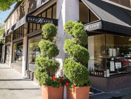 A corner view of a restaurant with a sign reading "Papa Haydn," featuring topiary plants and flower pots outside.