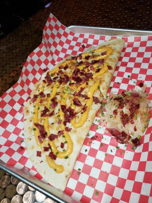 A folded flatbread topped with cheese, chopped meat, and drizzled sauce, served with a side of shredded cabbage.