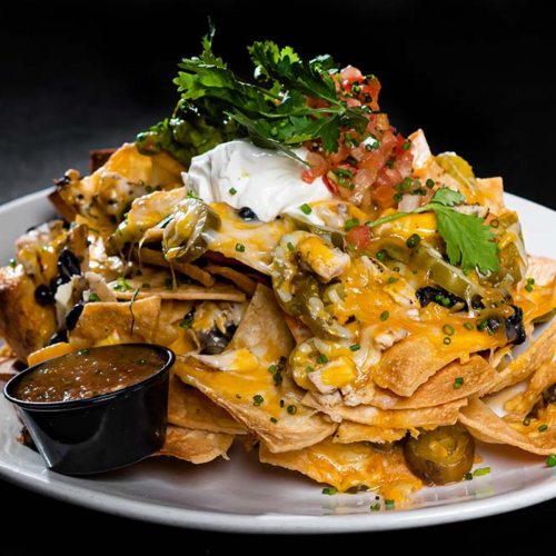 A plate of loaded nachos topped with cheese, jalapeños, sour cream, pico de gallo, and served with salsa.