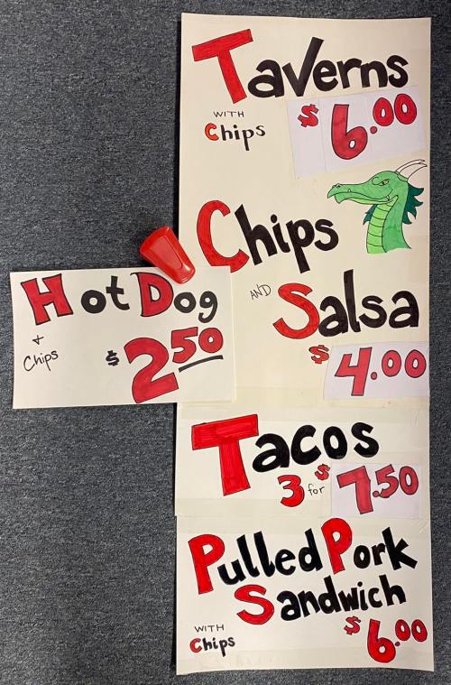 Menu signs featuring food items: Taverns $6, Hot Dog $2.50, Chips and Salsa $4, Tacos 3 for $7.50, Pulled Pork Sandwich $6.