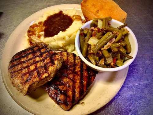 A plate featuring grilled meat, mashed potatoes with gravy, green beans, and a cornbread muffin.