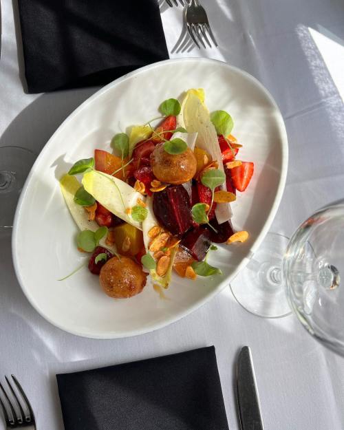 A vibrant salad with beets, greens, and crispy elements, served on a white plate with elegant table settings.