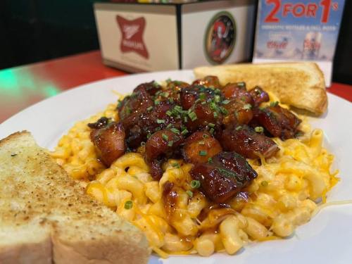 A plate of macaroni and cheese topped with diced barbecue chicken, garnished with green onions, and served with toast.