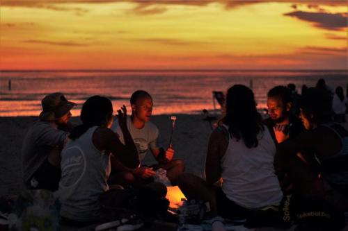 A group of people gathered around a small fire on the beach at sunset, sharing stories and enjoying the evening.