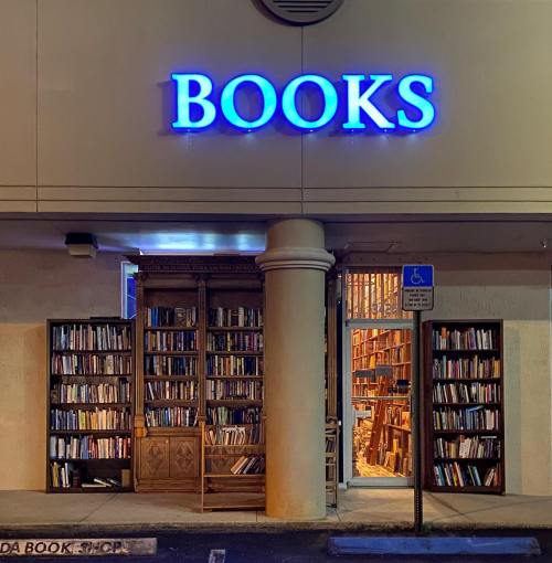 A bookstore entrance at night, featuring a large "BOOKS" sign and shelves filled with books visible inside.