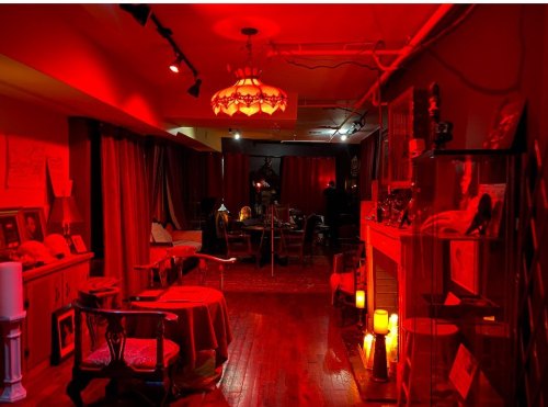 A dimly lit room with red lighting, featuring vintage furniture, a fireplace, and decorative items.