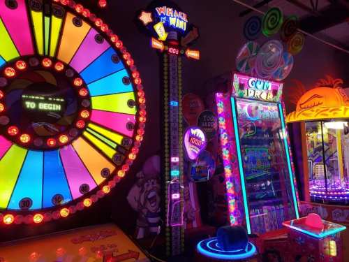Colorful arcade games with bright lights, including a spinning wheel and a ticket redemption machine.