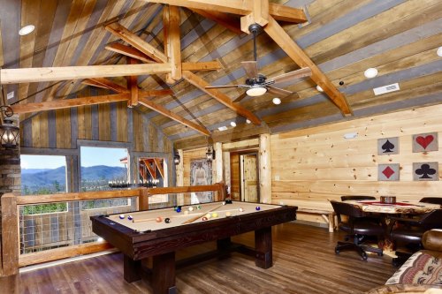 Cozy game room with a pool table, wooden beams, and large windows showcasing mountain views.