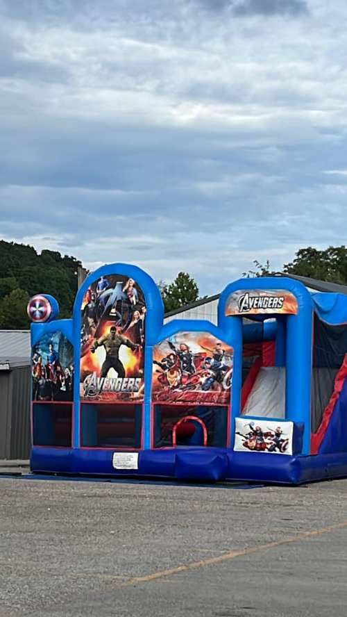 A colorful Avengers-themed bounce house set up outdoors, featuring superhero graphics and a slide.