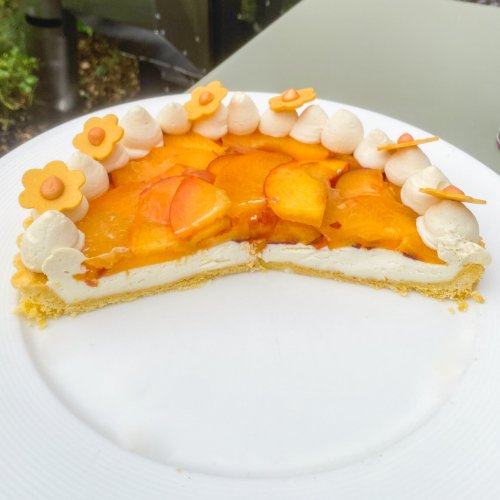 A sliced fruit tart with peach slices, cream, and decorative flowers on top, served on a white plate.