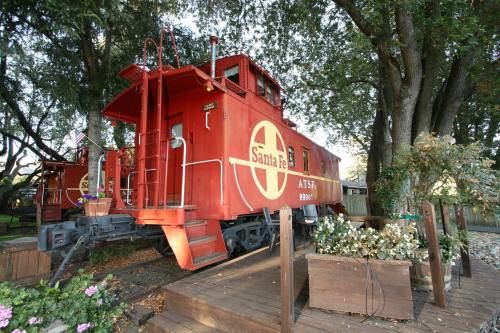 A red Santa Fe caboose parked on a wooden platform surrounded by greenery and flowers.