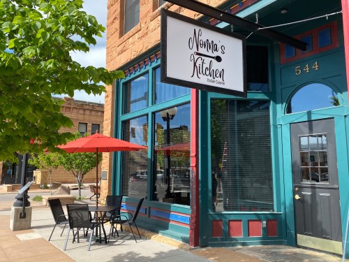 Exterior of Nona's Kitchen, an Italian restaurant, featuring a sign, outdoor seating, and a red umbrella.