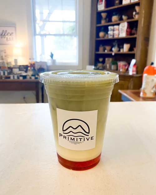 A layered drink in a clear cup with a logo, featuring green matcha on top and a red layer at the bottom.