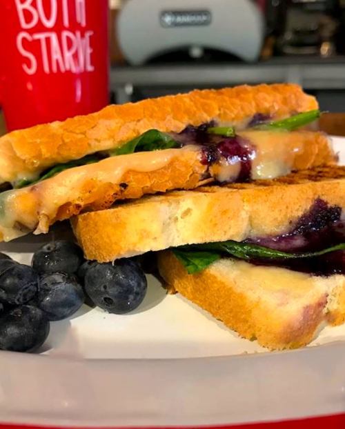 A plate with a grilled cheese sandwich filled with spinach and blueberry jam, accompanied by fresh blueberries.
