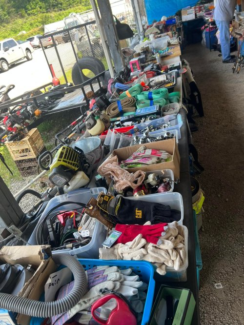A cluttered table filled with various tools, gloves, and equipment in a market setting.