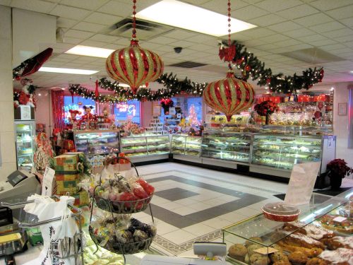 A festive bakery interior decorated for the holidays, featuring display cases filled with treats and colorful ornaments hanging.