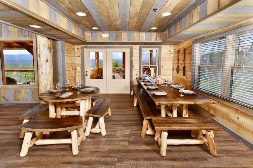 Rustic dining area with wooden tables and benches, large windows, and a door leading to an outdoor view.
