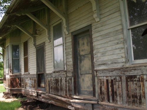 An old, weathered house with peeling paint and multiple doors, set on a slightly raised foundation.