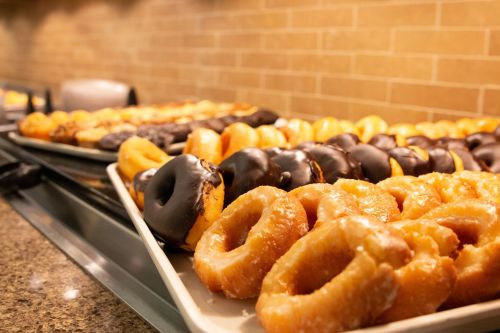 A variety of donuts displayed on trays, including glazed, chocolate-covered, and filled options.