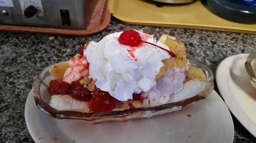 A banana split topped with whipped cream, a cherry, pineapple, strawberries, and granola in a glass dish.