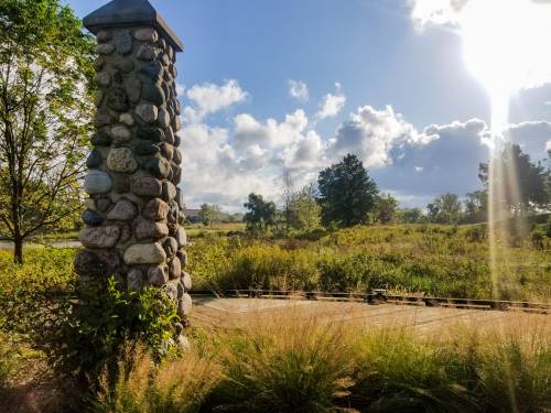 A stone pillar stands in a grassy field under a bright sky with clouds and sunlight streaming through.
