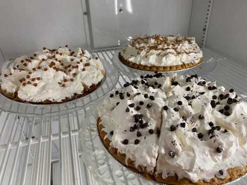 Three cream pies with whipped topping and chocolate chips, displayed on a shelf in a refrigerator.