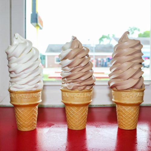 Three ice cream cones with swirled soft serve: one vanilla, one chocolate, and one half vanilla, half chocolate, on a red table.