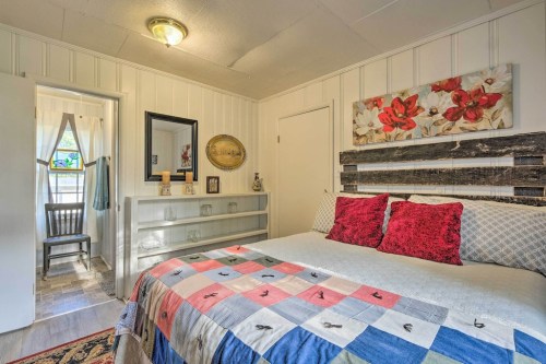 Cozy bedroom with a quilted bed, floral artwork, and a view of a bathroom through an open door.