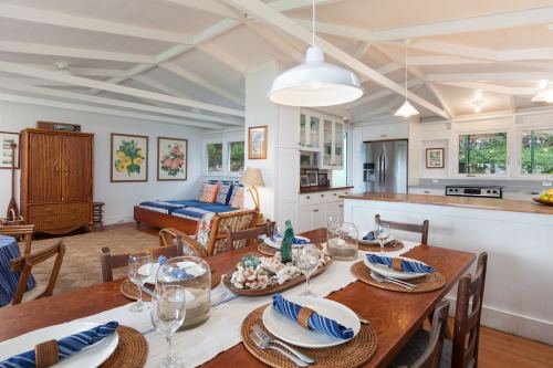 Bright, airy dining area with a wooden table set for a meal, featuring a cozy living space in the background.