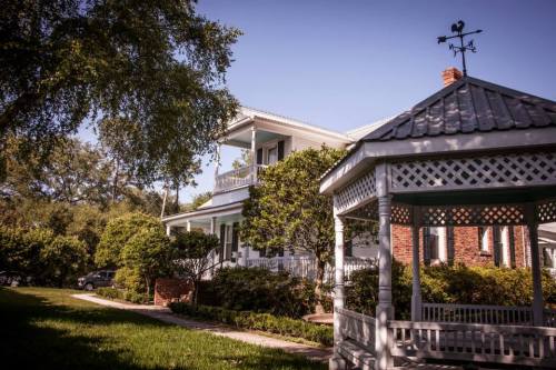 A charming white house with a gazebo in the foreground, surrounded by lush greenery and a clear blue sky.