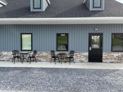 Exterior of a building with a gray facade, featuring stone accents and outdoor seating with black metal tables and chairs.