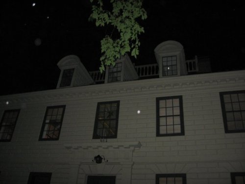 A dark night view of a historic house with a tree branch and visible windows, featuring a classic architectural style.