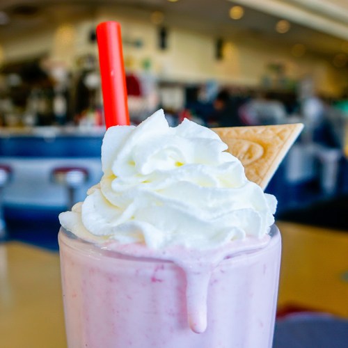 A close-up of a strawberry milkshake topped with whipped cream and a cookie, with a red straw.