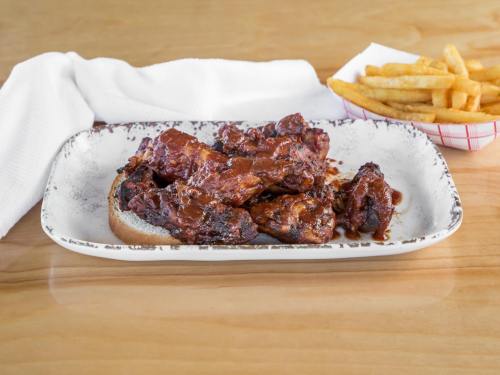 A plate of saucy chicken wings on bread, accompanied by a side of golden French fries.