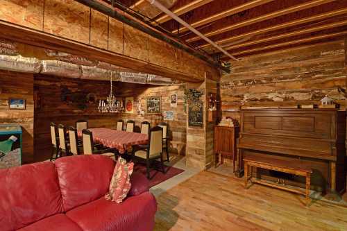 Cozy basement interior featuring a dining area, piano, and rustic wooden walls, with a red couch in the foreground.