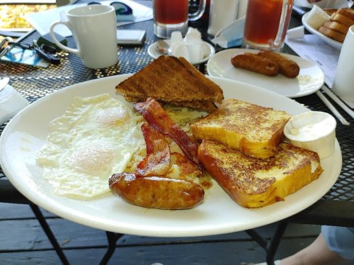 A plate of breakfast featuring eggs, bacon, sausage, French toast, and a side of cream.