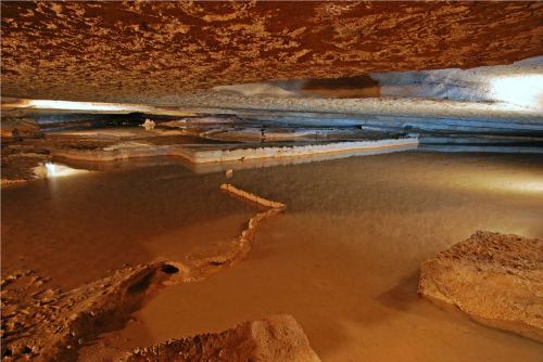 A serene underground cave with calm water reflecting the rocky ceiling and formations.