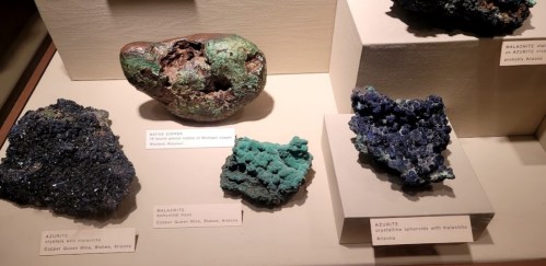 Display of various mineral specimens, including azurite and malachite, in a museum setting.